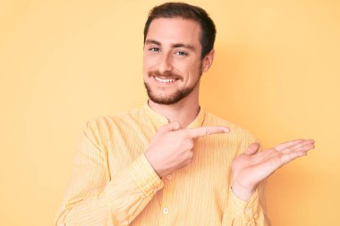 Gündelik kıyafetler giyen genç yakışıklı adam kameraya hayret ediyor ve gülümsüyor.. 