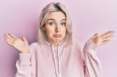 Gündelik kıyafetler giyen genç sarışın kız, habersiz ve kolları açık, hiçbir fikrim yok ve şüpheli bir yüz var.. 