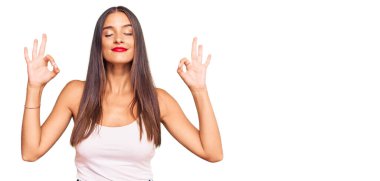 Gündelik kıyafetler giyen, gözleri kapalı gülümseyen genç İspanyol kadın parmaklarıyla meditasyon hareketi yapıyor. yoga konsepti. 