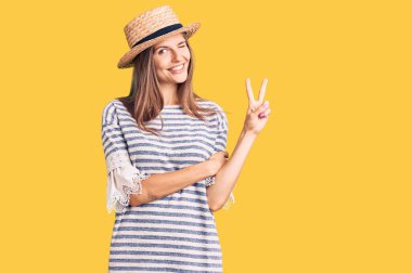 Yazlık şapkalı güzel beyaz kadın kameraya bakıp gülümsüyor ve zafer işareti yapıyor. İki numara.. 