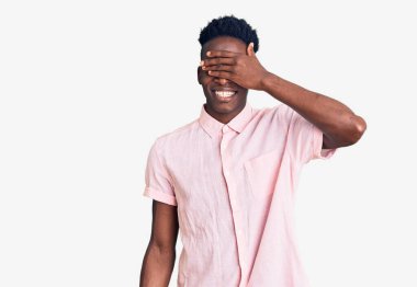 Sıradan kıyafetler giyen, gülümseyen ve gülen genç Afro-Amerikan erkeği şaşırtmak için gözlerini kapatıyor. kör kavram. 