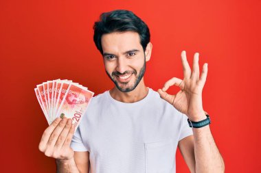 Genç İspanyol adam elinde 20 İsrail şekeri banknotları tutuyor. Parmaklarıyla imza atıyor, gülümsüyor. Mükemmel bir sembol. 