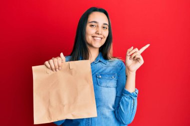 Elinde kağıt torba tutan genç İspanyol kadın gülümsüyor mutlu bir şekilde elini ve parmağını yana doğru gösteriyor. 
