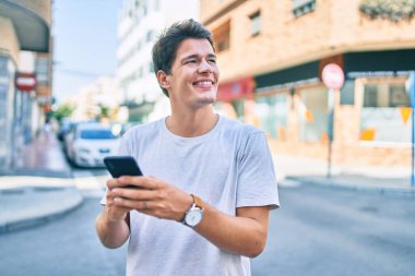 Beyaz adam şehirde akıllı telefon kullanarak mutlu bir şekilde gülümsüyor..