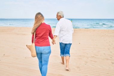 Orta yaşlı İspanyol çift kumsalda yürürken mutlu bir şekilde gülümsüyor..