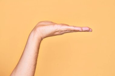 Beyaz bir gencin eli, izole edilmiş sarı arka plan üzerinde parmaklarını gösteriyor. Düz palmiye ürünü sunuyor, el hareketi yapıyor, boş kopya alanı veriyor.