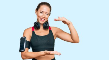 Güzel sarışın kadın spor kıyafetleri giyiyor ve kulaklık kullanıyor. Büyük ve büyük boylarda işaret eden el kol hareketleri yapıyor. Ölçüm sembolü. Kameraya bakıp gülümsüyor. ölçüm kavramı. 