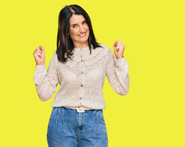 Orta yaşlı esmer kadın gündelik kıyafetler giyiyor gururla bağırıyor, zaferi kutluyor ve kollarını kaldırarak başarıyı kutluyor. 