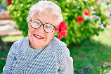 Yaşlı yaşlı, gri saçlı, dışarıda mutlu gülümseyen, dekoratif bir çiçek takan yaşlı kadın.