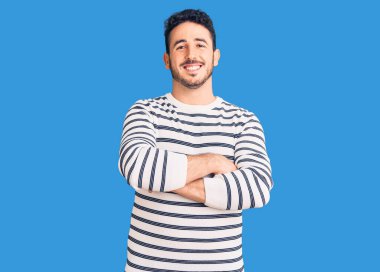 Gündelik kıyafetler giyen, kollarını kavuşturup kameraya gülümseyen genç İspanyol adam. pozitif kişi. 