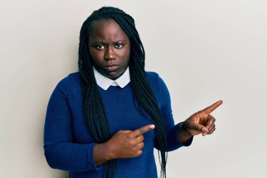 Saçları örgülü genç siyahi kadın parmaklarını yana çevirmiş şüpheci ve gergin, sorun yüzünden kaşlarını çatıyor. negatif kişi. 