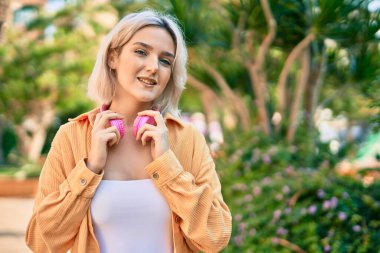 Parkta kulaklık takarak mutlu gülümseyen genç sarışın kız..