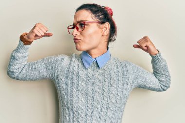 Sıradan kıyafetler ve gözlük takan beyaz bir kadın gururla gülümseyen kol kaslarını gösteriyor. fitness konsepti. 