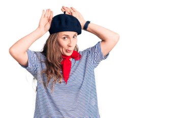 Fransız beresi takan, çizgili tişört giyen, tavşan kulağı yapan, avuçlarında alaycı ve şüpheci bakışlar olan genç, güzel sarışın kadın. Paskalya tavşanı konsepti. 