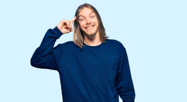 Uzun saçlı, sıradan bir süveter giyen yakışıklı beyaz adam tek parmağıyla kafasını gösteren gülümseme, harika bir fikir ya da düşünce, iyi bir hafıza 