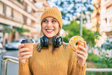 Genç sarışın kadın kulaklık takıyor ve şehirde kahvaltı yapıyor..