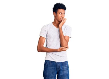 Gündelik beyaz tişört giyen Afro-Amerikalı genç bir adam gergin görünüyor ve elleri ağzında tırnak yiyor. anksiyete. 