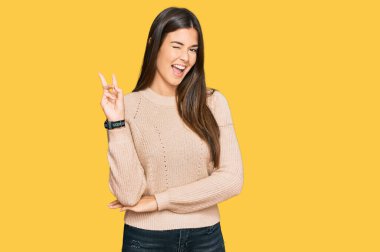 Kış süveteri giyen genç esmer kadın kameraya gülümseyen ve parmaklarıyla zafer işareti yapan. İki numara.. 