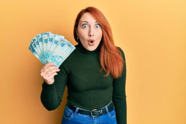 Güzel kızıl saçlı kadın elinde 100 Brezilyalı gerçek banknot tutuyor. Şaşırmak için ağzı açık, korkmuş ve hayrete düşmüş. İnanmayan yüz. 
