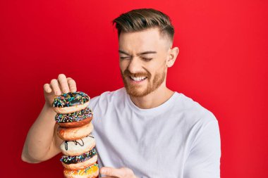 Genç kızıl saçlı adam elinde lezzetli renkli çöreklerle gülüyor ve kahkahalarla gülüyor.. 