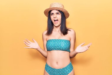 Bikini ve yaz şapkası giyen genç ve güzel bir kız. Deli gibi bağırıyor, agresif bir ifadeyle bağırıyor ve kollarını kaldırıyor. hüsran kavramı. 