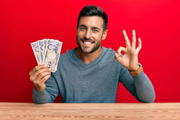 日本円の紙幣を持っているハンサムなヒスパニック系の男性は 指でOkサインをし 優れたシンボルをジェスチャー笑顔 — ストック写真