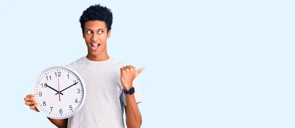 Młody Afrykanin Amerykański Człowiek Trzyma Duży Zegar Wskazując Kciuk Górę — Zdjęcie stockowe