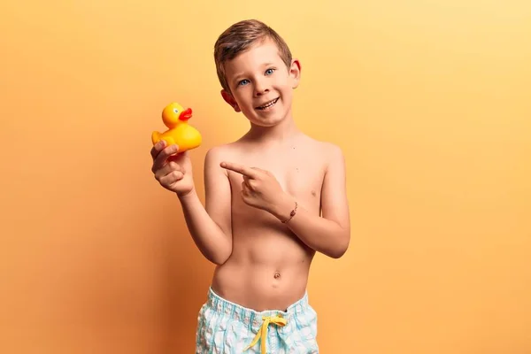 可爱的金发碧眼的孩子穿着泳衣牵着鸭玩具开心地微笑着 用手和手指指指点点着 — 图库照片