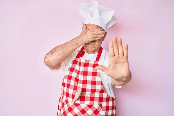 年长的白发男子 身穿职业面包师围裙 用手捂住眼睛 以忧郁和恐惧的表情做停止动作 尴尬和消极的概念 — 图库照片