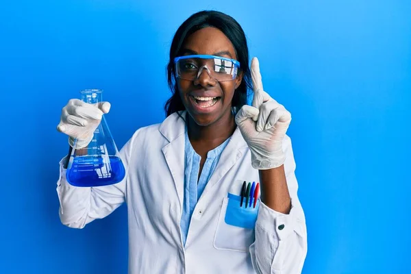 若いアフリカ系アメリカ人女性を身に着けている科学者の制服保持テスト管笑顔でアイデアや質問を指差す指で幸せな顔 ナンバーワン — ストック写真
