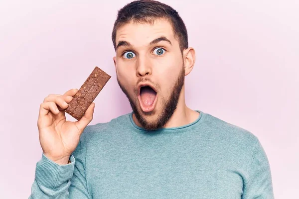 Jovem Homem Bonito Segurando Barra Proteína Assustado Surpreso Com Boca — Fotografia de Stock