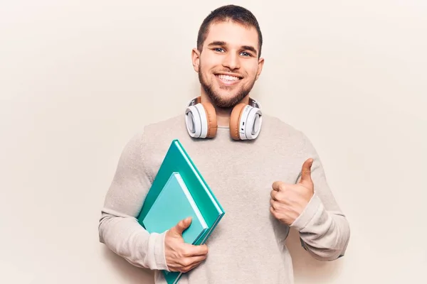 Jovem Homem Bonito Segurando Livro Usando Fones Ouvido Sorrindo Feliz — Fotografia de Stock