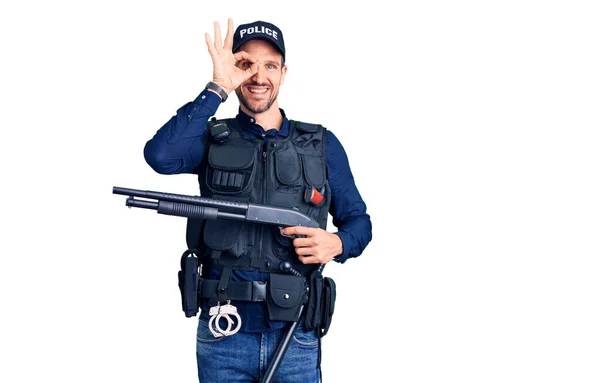 年轻英俊的男子身穿警服 手持霰弹枪 手拿着手签 微笑着表示友善的手势 象征着优秀的象征 — 图库照片