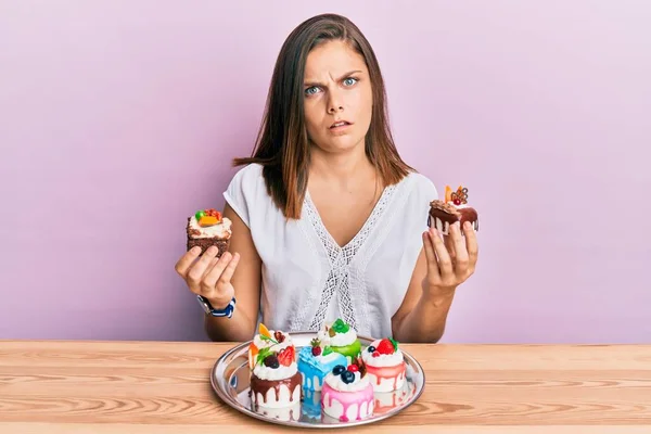 ケーキのスライスを持っている若い白人女性は無知で混乱した表情 疑わしい概念 — ストック写真