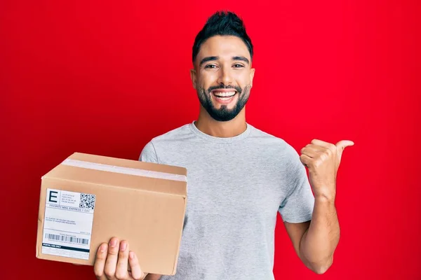 Young Man Beard Holding Delivery Package Pointing Thumb Side Smiling — Stock Photo, Image