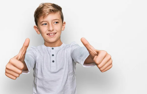 手で積極的なジェスチャーを行うことを承認カジュアル服を身に着けている小さな白人の男の子 親指アップ笑顔と成功のために幸せ 勝者のジェスチャー — ストック写真