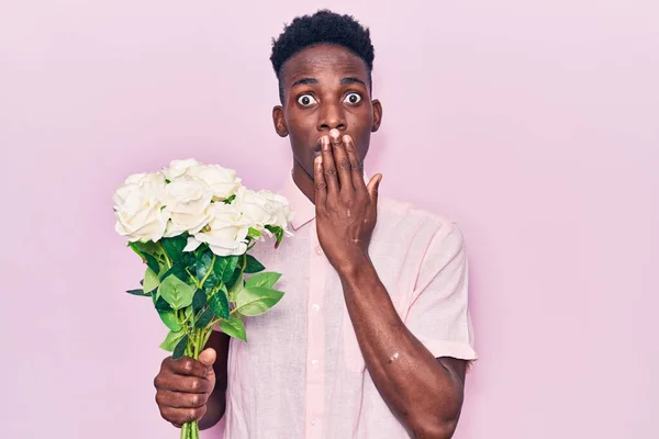 Joven Hombre Afroamericano Sosteniendo Flores Cubriendo Boca Con Mano Sorprendido — Foto de Stock