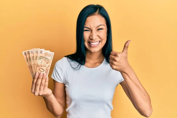 Beautiful Hispanic Woman Holding Brazilian Real Banknotes Smiling Happy Positive — 스톡 사진