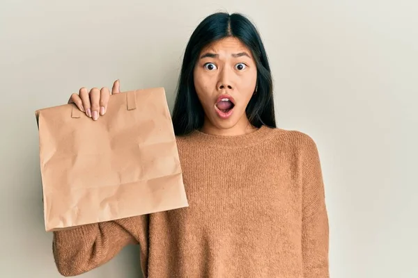 若い中国人女性を持って紙の袋を離れて怖がって驚きのために口を開けて驚いて 不信の顔 — ストック写真