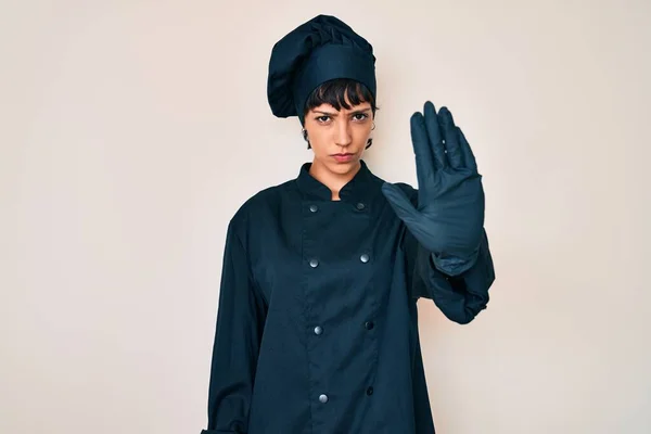 Beautiful brunettte woman wearing professional cook uniform doing stop sing with palm of the hand. warning expression with negative and serious gesture on the face.
