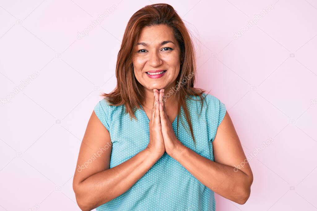 Middle age brunette hispanic woman wearing casual clothes praying with hands together asking for forgiveness smiling confident. 