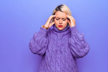 Güzel sarışın ve cüsseli bir kadın mor arka plan üzerine balıkçı yaka kazak giyiyor ve baş ağrısı çekiyor. Migren ağrısı..