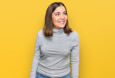 Balıkçı yaka kazak giyen genç ve güzel bir kadın yüzünde gülümsemeyle yan yana bakıyor, doğal bir ifade. Kendinden emin gülen. 