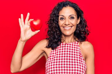 Orta yaşlı, kalbi olan güzel bir kadın. Pozitif ve mutlu görünüyor. Kendine güvenen bir gülümsemeyle ayakta duruyor ve dişlerini gösteriyor. 