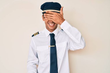 Uçak pilotu üniforması giyen genç İspanyol bir adam. Gülümsüyor ve elleri yüzünde gülüyor. Şaşırtmak için gözleri örtüyor. kör kavram. 