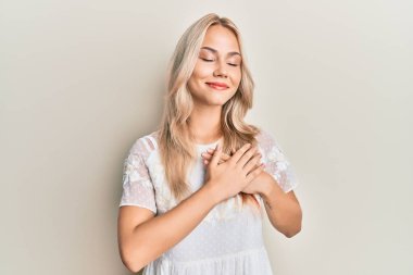 Beyaz tişörtlü, göğsünde elleri göğsünde, yüzünde minnet dolu bir jest ile gülümseyen güzel beyaz sarışın kız. sağlık kavramı. 