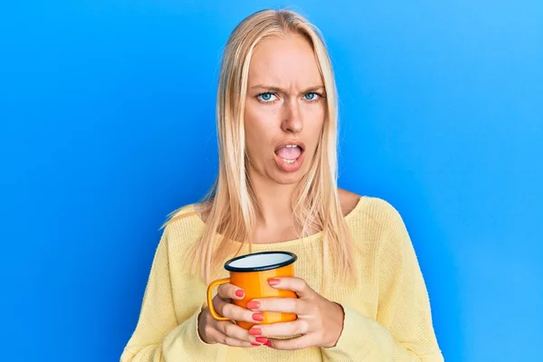 Ung Blond Flicka Som Håller Kaffe Chockansikte Ser Skeptisk Och — Stockfoto