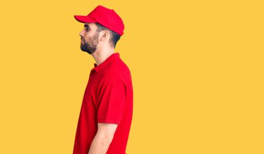 Sakallı yakışıklı bir adam teslimat üniforması giyiyor. Taraf arıyor, rahat bir görünüm takınıyor ve kendine güvenen bir gülümsemeyle poz veriyor.. 