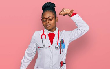 Genç Afro-Amerikan kadın doktor üniforması ve steteskop giyiyor, yorgun ve rahat, uykulu ve sabahın erken saatleri için esniyor. 