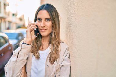 Beyaz kadın gülümsüyor. Şehirdeki akıllı telefondan konuşuyor..